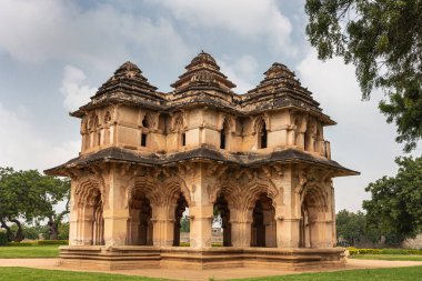 Hampi, Karnataka, Hindistan - 5 Kasım 2013: Zanana Enclosure. Kahverengi taştan yapılmış Lotus Mahal binasına yakın çekim. Yeşil parktaki mavi bulutların altında. Kenarlarında yeşil yapraklar.