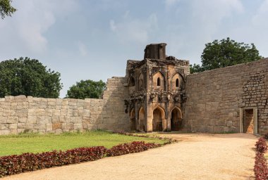 Hampi, Karnataka, Hindistan - 5 Kasım 2013: Zanana Enclosure. Kahverengi taş, mavi gökyüzünün altındaki doğu gözetleme kulesini harap ediyor. Yeşil yapraklar ve kırmızı yapraklı çimenler..