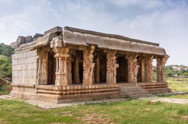Hampi, Karnataka, Hindistan - 5 Kasım 2013: KudureGombe mandapam ve antik kuyu. Mavi bulutların altında yeşil ortamda kurulmuş kahverengi taş binanın yakınına. At heykelleri..