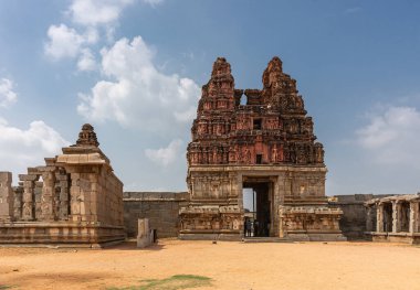 Hampi, Karnataka, Hindistan - 5 Kasım 2013: Vijaya Vitthala Tapınağı. Sarı taş kapı tabanında kırmızı Gopuram mavi bulutların altında kumlu bir avludan görüldü. Diğer yapılar harap..