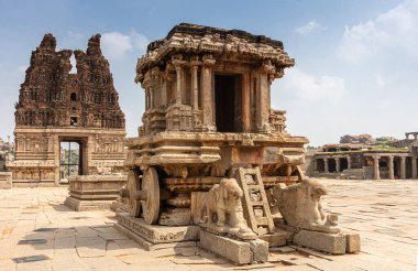 Hampi, Karnataka, Hindistan - 5 Kasım 2013: Vijaya Vitthala Tapınağı. Kahverengi taştan savaş arabasının önü mavi bulutların altında, doğu Gopuram 'ın arka tarafı kırmızı..