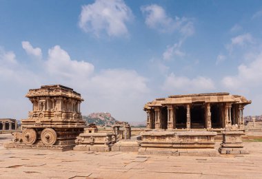 Hampi, Karnataka, Hindistan - 5 Kasım 2013: Vijaya Vitthala Tapınağı. Savaş arabası ve mavi bulutların altında boş harabe mandallar. Boulder tepesi ufukta.
