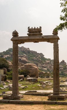 Hampi, Karnataka, Hindistan - 5 Kasım 2013: Antik Tapınak. Bej renkli taşın portresi. Gümüş gökyüzünün altında kahverengi taşlarla dolu yeşil tepeli, serbest duran bir kapı.. 