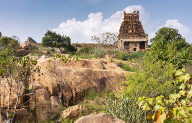 Hampi, Karnataka, Hindistan - 5 Kasım 2013: Malyavanta Raghunatha Tapınağı. Güney Gopuram 'da kayaların, yeşil otların ve mavi bulutların altındaki ağaçların üzerinde tek başına kahverengi bir taş görülüyor..