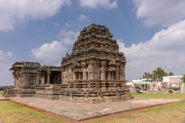 Lakkundi, Karnataka, Hindistan - 6 Kasım 2013: Kahverengi taş Kasivisvesvara Tapınağı yeşil çimlerin arkasında mavi bulutların altında. Arka taraftaki ikametgah..