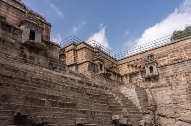 Lakkundi, Karnataka, Hindistan - 6 Kasım 2013: Musakeena Bhavi basamak tankı. Kahverengi taş merdiven boşluğunda geniş bir köşe. Mavi bulutların altında gözden kaçan oyuklar var..