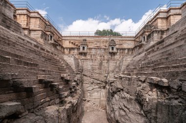 Lakkundi, Karnataka, Hindistan - 6 Kasım 2013: Musakeena Bhavi basamak tankı. Kahverengi taşlar ve kayalarla çevrili derin ve kuru kuyunun dibinden geniş bir manzara. Mavi bulut.