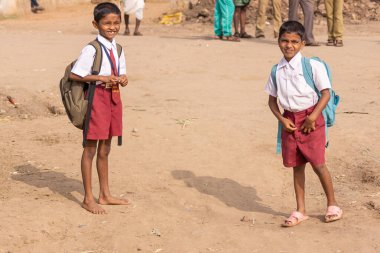 Nandakeshwar, Karnataka, Hindistan - 7 Kasım 2013: Kumlu kumlu yolda, kestane rengi şortlar ve beyaz gömleklerle okula giden iki erkek çocuğu.