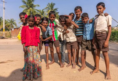 Siddanakolla, Karnataka, Hindistan - 7 Kasım 2013: Çoğunluğu erkek ve bir kız olmak üzere bir grup çocuk, mavi gökyüzünün altındaki kahverengi toprak üzerinde birlikte duruyorlar. Yeşil palmiye yaprağı.