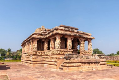 Aihole, Karnataka, Hindistan - 7 Kasım 2013: Kahverengi taş Durga Gudi 'nin Mandapam tarafı. Yanlarda yeşil yapraklar. Sütunlardaki heykeller.