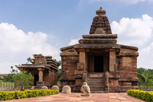 Aihole, Karnataka, Hindistan - 7 Kasım 2013: Huchchimalli Gudi veya Temple. Kahverengi taş ana bina. Mavi bulutların altında bitişik küçük bir türbe ve arkasında yeşil yapraklar var. Nandi heykeli.