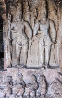 Aihole, Karnataka, Hindistan - 7 Kasım 2013: Ravanaphadi Mağarası Shiva Tapınağı. İki gri taştan heykel, bir sıra küçük figürün üzerinde duran insan figürleri..