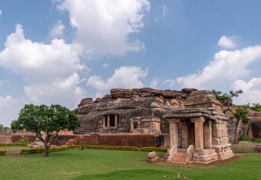Aihole, Karnataka, Hindistan - 7 Kasım 2013: Ravanaphadi Mağarası Shiva Tapınağı. Kahverengi taş tapınak alımları ve mavi bulutların altında siyah kaya mağarası olan yeşil bir arazi..