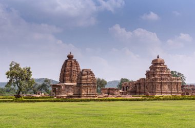 Bagalakote, Karnataka, Hindistan - 7 Kasım 2013: Pattadakal Tapınağı Kompleksi. Geniş Yeşil Park manzarası. Kahverengi taş binaların kompleksi mavi bulutların altında birleşiyor..