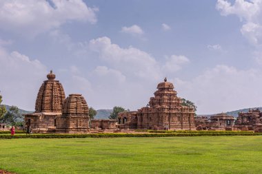Bagalakote, Karnataka, Hindistan - 7 Kasım 2013: Pattadakal Tapınağı Kompleksi. Kahverengi taştan binaların kompleksiyle yeşil park manzarası mavi bulutların altında bir arada..