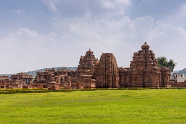 Bagalakote, Karnataka, Hindistan - 7 Kasım 2013: Pattadakal Tapınağı Kompleksi. Kahverengi taş tapınak binalarının duvarı mavi bulutların altında birleşip yeşil parka kurulmuş..