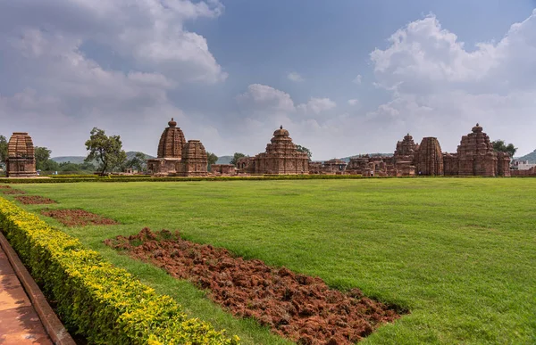 Bagalakote, Karnataka, Hindistan - 7 Kasım 2013: Pattadakal Tapınağı Kompleksi. Mavi bulutların altında kahverengi binalar ve önünde toprak olan yeşil çimenler üzerinde geniş bir manzara..