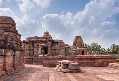 Bagalakote, Karnataka, Hindistan - 7 Kasım 2013: Pattadakal Tapınağı Kompleksi. Kahverengi taş Viriupaksha ve Jambulingeshwar tapınağı birleşimi mavi bulutların altında yeşil yapraklar.