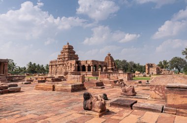 Bagalakote, Karnataka, Hindistan - 7 Kasım 2013: Pattadakal Tapınağı Kompleksi. Mavi bulutların altındaki kahverengi taş harap tapınak binalarına bakın. Hasarlı Nandis ve yeşil yapraklar ortada..