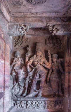 Badami, Karnataka, Hindistan - 7 Kasım 2013: Agasthya Gölü üzerindeki mağara tapınakları. Kırmızımsı Ardhanarishvara heykeli, Shiva ve Parvati kombinasyonu. Nandi ve Bhringi, sola. Hizmetçi sağdan mücevher getiriyor..