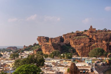 Badami, Karnataka, Hindistan - 7 Kasım 2013: Agasthya Gölü üzerindeki mağara tapınakları. Kızıl kayalıkların önündeki şehir manzarası. Mavi bulutların altında Yukarı Shivalaya tapınağı var.,