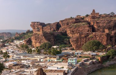 Badami, Karnataka, Hindistan - 7 Kasım 2013: Agasthya Gölü üzerindeki mağara tapınakları. Kızıl kayalıkların önündeki şehir manzarası. Mavi bulutların altında Yukarı Shivalaya tapınağı var.,