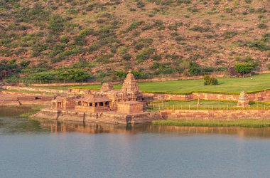 Badami, Karnataka, Hindistan - 7 Kasım 2013: Bhootnath Tapınağı ve onun Agasthya Gölü 'nün doğu kıyısındaki yeşil çimlerinin kapatılması. Günbatımının altında kızıl kaya tepeleri. 