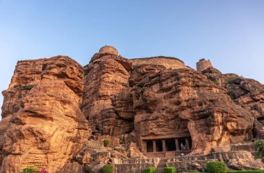 Badami, Karnataka, Hindistan - 7 Kasım 2013: Agasthya Gölü üzerindeki mağara tapınakları. İlk mağaranın girişi, mavi gökyüzünün altında istihkamlarla kırmızı kaya kayalıklarına kesiliyor..