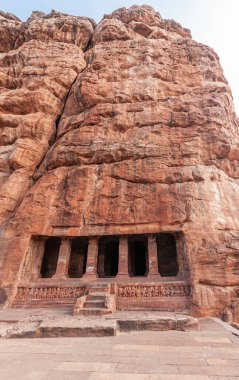 Badami, Karnataka, Hindistan - 7 Kasım 2013: Agasthya Gölü üzerindeki mağara tapınakları. Kırmızı kaya kayalıklarına açılan ikinci mağara girişinde sütunlar ve basamaklar görülüyor..