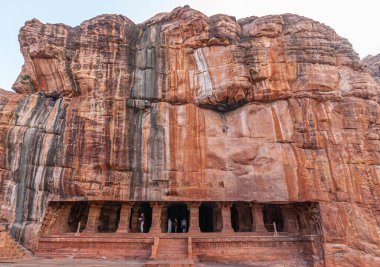 Badami, Karnataka, Hindistan - 7 Kasım 2013: Agasthya Gölü üzerindeki mağara tapınakları. Kırmızı kaya kayalıklarına açılan üçüncü mağara girişinde sütunlar ve basamaklar görülüyor..