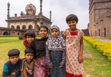 Vijayapura, Karnataka, Hindistan - 8 Kasım 2013: İbrahim Rauza. Arkadaki camii olan yeşil çimlerde renkli giyinmiş bir grup çocuk..