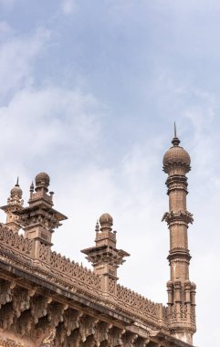 Vijayapura, Karnataka, Hindistan - 8 Kasım 2013: Kahverengi taş NE köşe minaresi ve mavi bulutlar altında İbrahim Rauza camiinin çatı heykelleri. 