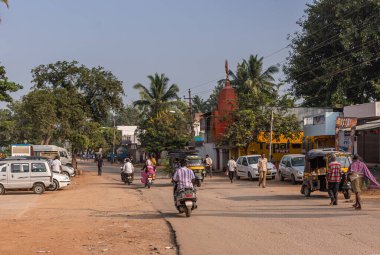 Patel Nagar, Karnataka, Hindistan - 9 Kasım 2013: Yayalar ve motorlu trafik ile ana cadde manzarası. Farklı renklerde küçük binalar ve mavi gökyüzünün altında yeşil ağaçlar..