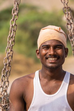 Ayodhya, Karnataka, Hindistan - 9 Kasım 2013: Gülümseyen genç çiftçinin portresi, türban ve beyaz atlet giymektedir. Terazinin zincirlerinde duruyor.