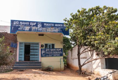 Ballapur, Karnataka, Hindistan - 9 Kasım 2013: Pragathi Gramin Bank binası, açık mavi gökyüzü altında yeşil yapraklar ve kahverengi toprakla kaplı küçük bir yerel şubedir..