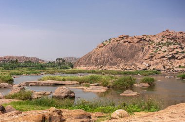 Anegundi, Karnataka, Hindistan - 9 Kasım 2013: Navabrindavana Adası ve Tapınağı. Tungabhadra nehir manzarası bol yeşillik ağaçlar ve su havuzlarının etrafındaki yabani otlar ve kaya parçaları..