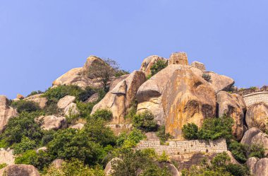 Chitradurga, Karnataka, Hindistan - 10 Kasım 2013: Fort veya Elusuttina Kote. Kahverengi taştan duvar, mavi gökyüzünün altından yeşil yapraklarla kayalık tepeyi kesiyor..