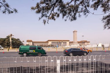 Pekin, Çin - 27 Nisan 2010: Tiananmen boyunca uzanan Büyük Halk Salonu açık mavi gökyüzünün altında, önünde araba trafiği olan bir meydan. Savaş anıtı ve yeşil yaprakların dikilitaşı.