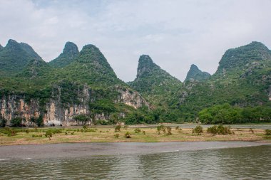 Guilin, Çin - 10 Mayıs 2010: Li Nehri boyunca. Geniş bir arazi, kısmen batık düz bataklık, orman sırtı dağ tepesi ve açık mavi gökyüzü altında siyah bej kayalıklar..