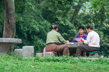 Guilin, Çin - 11 Mayıs 2010 Yedi Yıldız Parkı. Kadın ve iki erkek yeşil yapraklarla çevrili taş masada kağıt oynuyorlar..