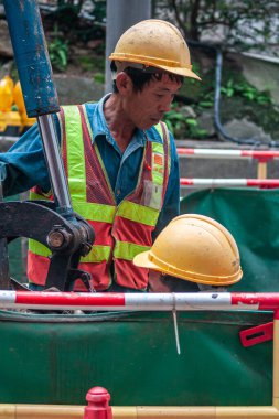 Hong Kong Adası, Çin - 14 Mayıs 2010: Yeşil branda ile korunan bir çukurda çalışan sarı kasklı, mavi gömlekli ve kırmızı-sarı yelekli inşaat işçilerinin yakınlaşması.