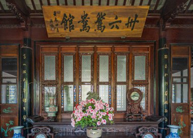 Suzhou, Çin - 3 Mayıs 2010: Mütevazı Yöneticiler Bahçesi. Çiçek buketi, vazolar ve sanat eserleriyle dolu karanlık ahşap açık oda Mandarin senaryosuyla büyük bir panonun altında sergileniyor.. 