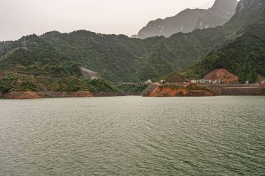 Yangtze Nehri, Three Gorges, Çin - 6 Mayıs 2010: Zigui bölgesi. Yeşil suyu olan geniş bir arazi, gümüş gökyüzünün altında yeşil, yoğun dağ yamaçları. Beton köprü, kızıl kaya kıyılarını binalara bağlıyor..