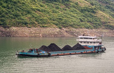 Yangtze Nehri, Three Gorges, Çin - 6 Mayıs 2010 Xiling Vadisi yakınlarında. Kıyı şeridinde yeşil ormanlı dağ yamacı olan yeşil sularda mavi siyah kömür nakliye mavnasına yakın çekim.