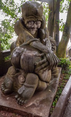 Fengdu, Çin - 8 Mayıs 2010 Hayalet Şehir, tarihi sığınak. Keskin dişleri olan yaşlı bir adamın kahverengi taş heykeli. Genç bir bayanın arkasında çıplak gezmekten hoşlanıyor gibi görünüyor. Yeşil yaprak.