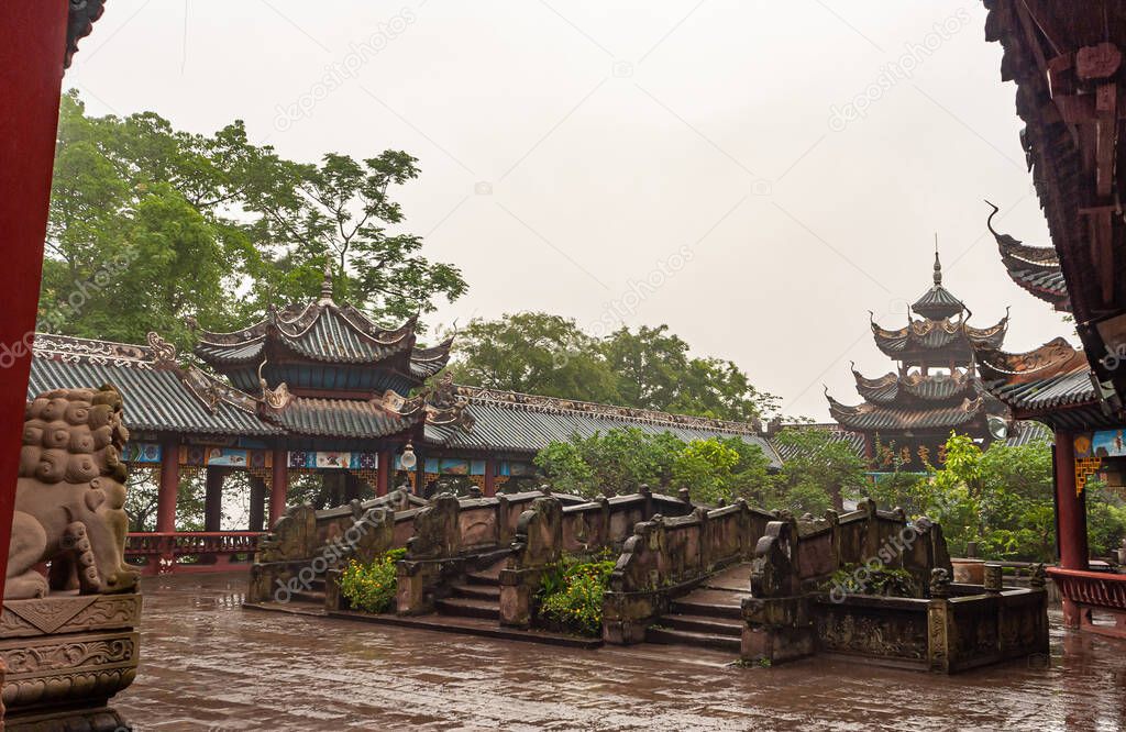 Fengdu, China - May 8, 2010: Ghost City, historic sanctuary. Wet rainy stone surfaces of bridges with Pagoda roof structures around in combo with green foliage under silver sky.