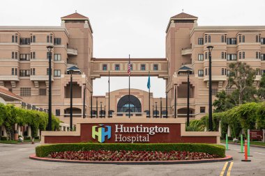 Pasadena, CA, ABD - 11 Mayıs 2021: Gümüş gökyüzünün altındaki bej rengi taştan Huntington Hastanesi 'nin önündeki ana giriş. Renkli amblem ve yeşil yapraklı çiçekler.