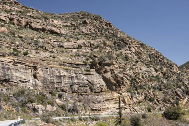 Los Padres Ulusal Ormanı, CA, ABD - 8 Nisan 2010: Mavi gökyüzünün altındaki dağın yamacında her şekilde kahverengi kayalık kayalık ve taşlar. Yol 33 en altta. Yeşil bitki örtüsü.