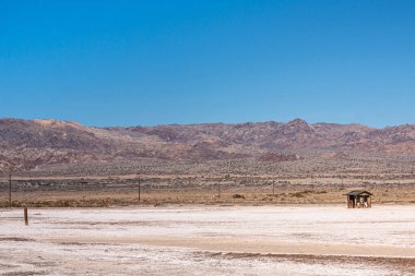 ABD, CA, Salton Denizi - 28 Aralık 2012: SE kıyı şeridi ufuk çizgisi üzerinde dağlar ve mavi gökyüzü olan Whtie Beach 'te izole edilmiş küçük harabe bir kulübe.