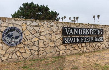 Lompoc, CA, USA - 26 Mayıs 2021: Vandenberg Uzay Üssü. Siyah tabeladaki beyazın dik açılı yakın çekimi ve açık mavi gökyüzünün altındaki çimlerin üzerindeki bej duvardaki amblem. Arkadaki yeşil ağaç..